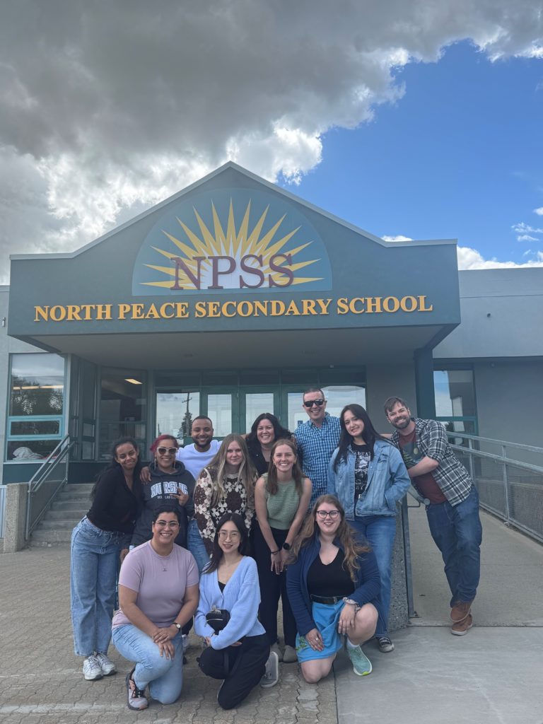 Health Professionals from the Healthcare Travelling Roadshow pose in front of the main doors at North Peace Secondary School. 