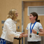 Board Chair Helen Gilbert congratulates one of the 2026 District Speech Contest top 3. Photo credit Adam Winn